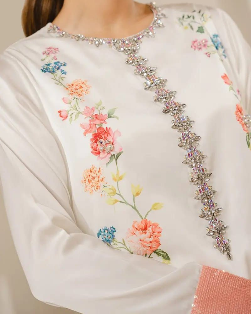 Close-up of a white garment with floral embroidery and decorative elements.