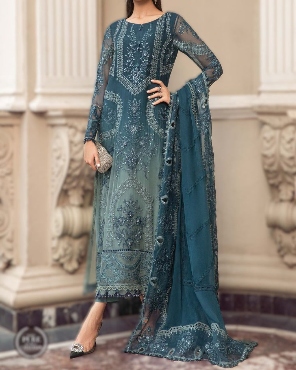 Teal embroidered outfit with matching dupatta against a decorative wall background