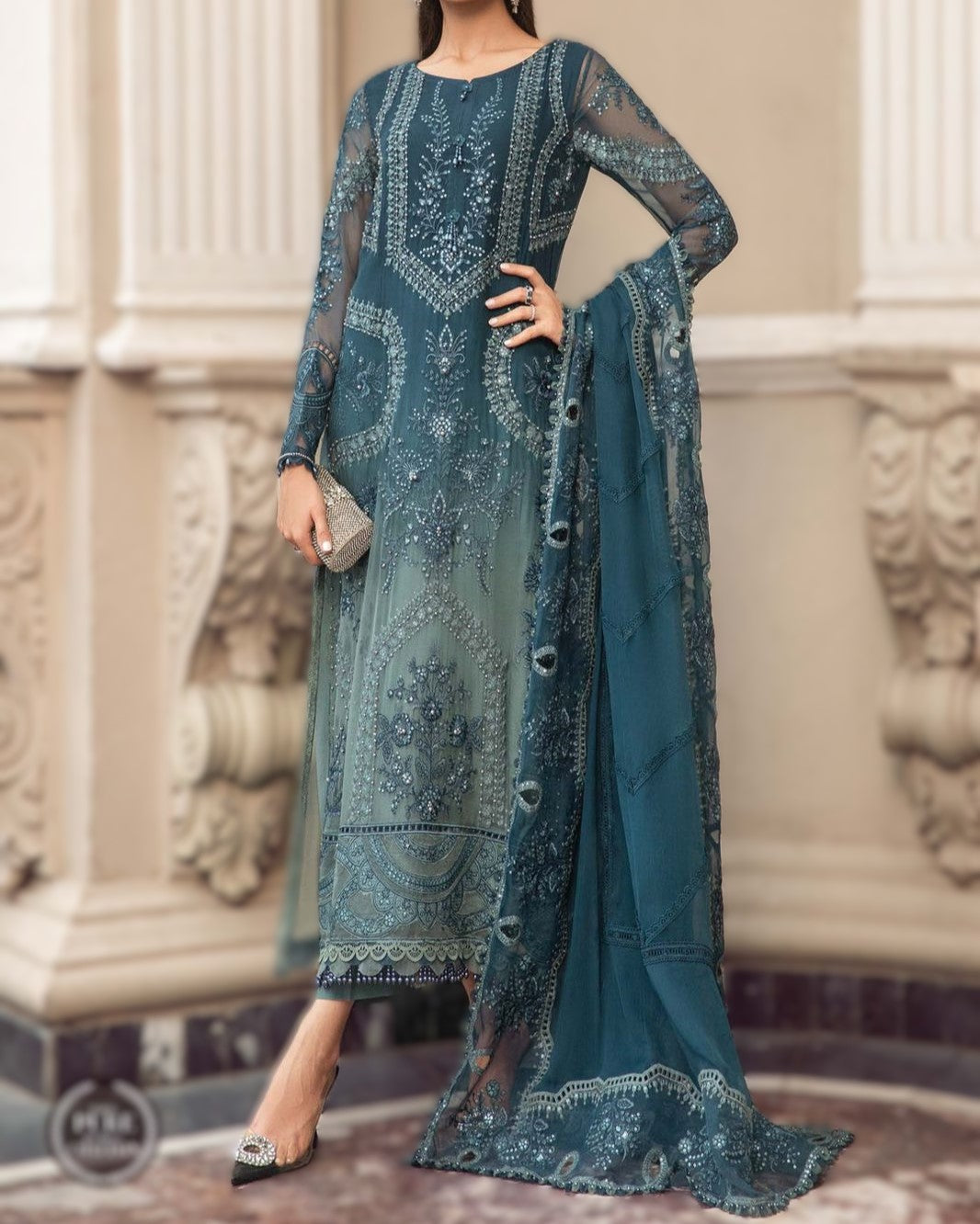 Teal embroidered outfit with matching dupatta against a decorative wall background